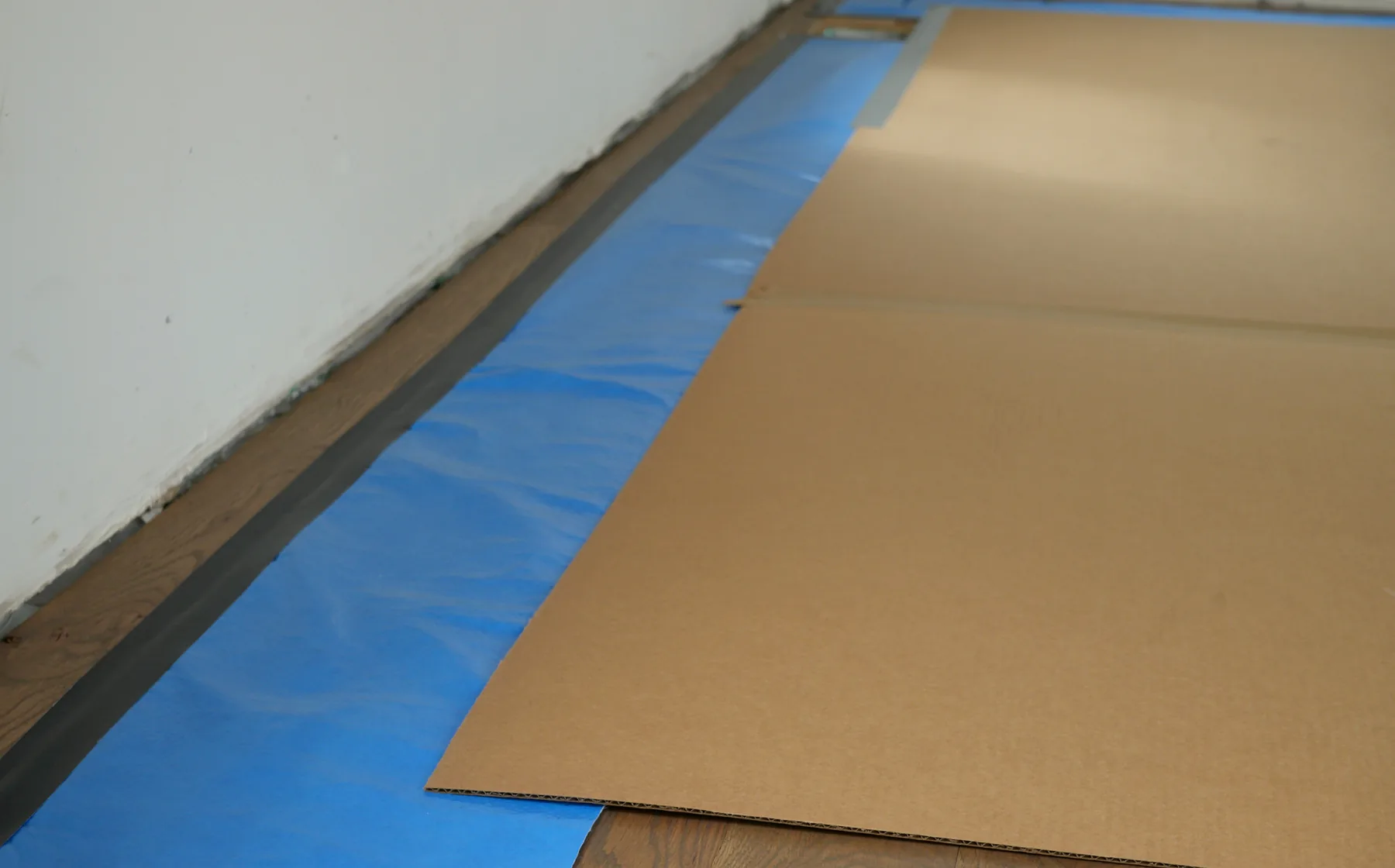 Layered floor protection showing finished floor, blue perimeter layer, taped edge, and cardboard field protection